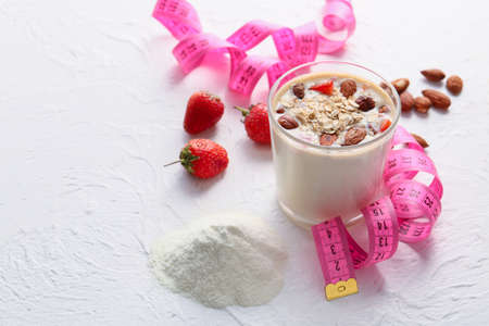 Glass of protein shake with measuring tape on white background