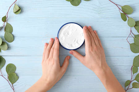 Hands of young woman and jar of cream on wooden backgroundの写真素材