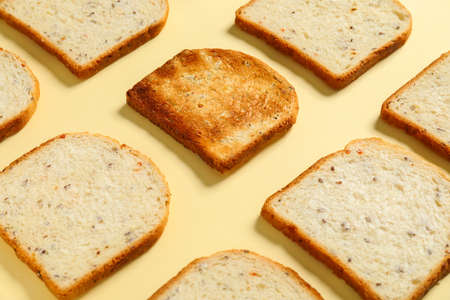 Toasted bread among fresh ones on color background. Concept of uniqueness