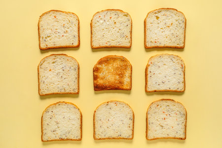 Toasted bread among fresh ones on color background. Concept of uniqueness