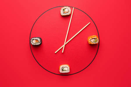 Creative clock made of tasty sushi and chopsticks on color backgroundの写真素材