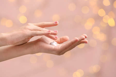 Beautiful young woman applying hand cream against color background with defocused lightsの写真素材