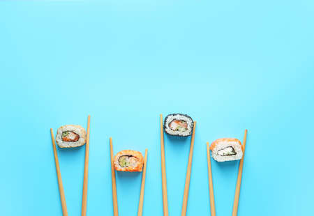 Tasty sushi rolls and chopsticks on color backgroundの写真素材