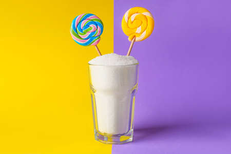Glass with sugar and lollipops on color background