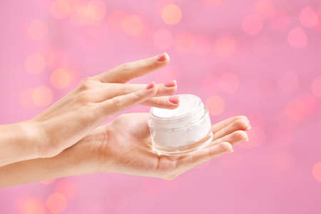 Female hands with jar of cream against color background with defocused lightsの写真素材