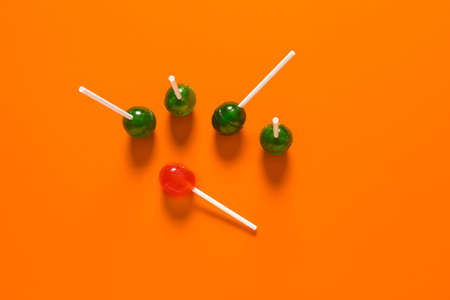 Orange lollipop among green ones on color background. Concept of uniquenessの写真素材