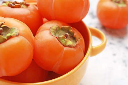 Pot with ripe persimmons on light background, closeupの写真素材
