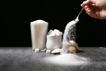 Woman pouring sugar from spoon onto tableの写真素材