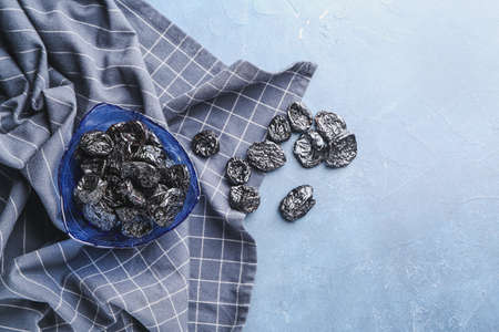 Bowl with tasty prunes on color background