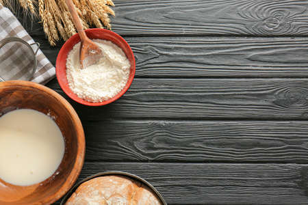 Bowls with flour and milk on dark table