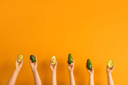 Female hands with fresh avocados on color backgroundの写真素材