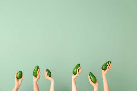Female hands with fresh avocados on color backgroundの写真素材