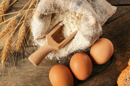 Bag with flour and eggs on wooden table