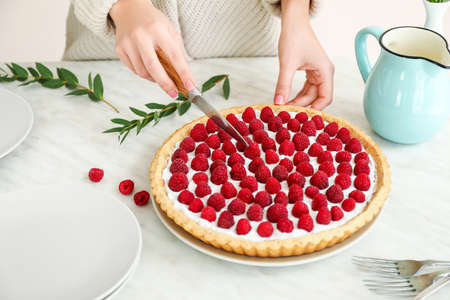 Woman cutting tasty raspberry pie on tableの写真素材