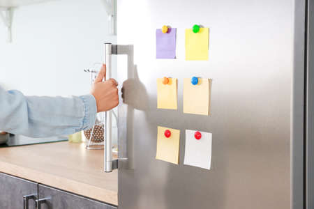 Woman opening modern fridge with stickers on door in kitchen