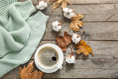 Warm sweater, cup of coffee, autumn leaves and cotton flowers on wooden backgroundの写真素材