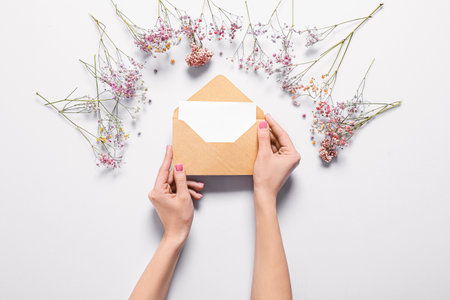 Female hands with envelope, invitation and flowers on white background, top viewの写真素材