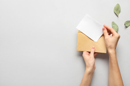 Female hands with envelope and invitation on light background, top viewの写真素材