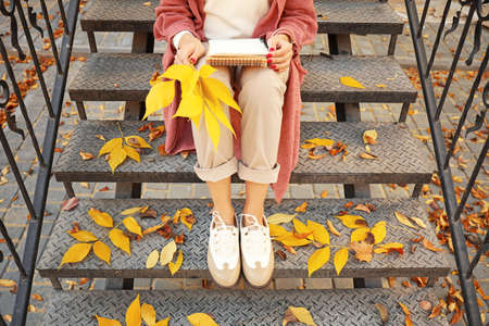 Beautiful young woman sitting on steps outdoors on autumn dayの写真素材