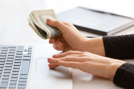 Woman with dollar banknotes using laptop at tableの写真素材