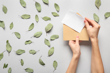 Female hands with envelope and invitation on light background, top viewの写真素材