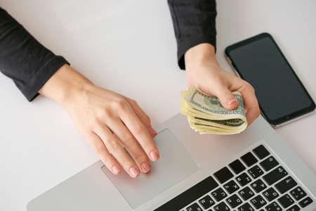 Woman with dollar banknotes using laptop at tableの写真素材