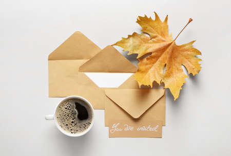 Invitation with envelopes and cup of coffee on light background