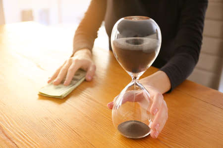 Woman with hourglass and money sitting at table, closeup