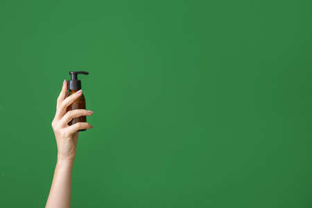 Female hand with cosmetic product in bottle on color background