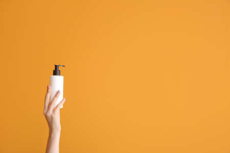Female hand with cosmetic product in bottle on color background