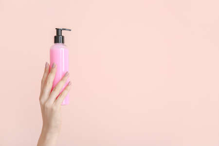 Female hand with cosmetic product in bottle on color backgroundの写真素材