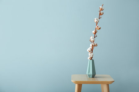 Vase with beautiful cotton flowers on table against color backgroundの写真素材