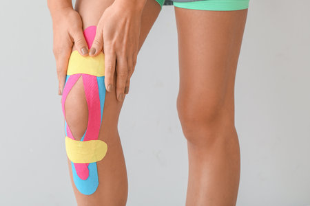 Sporty woman with physio tape applied on knee against light background, closeupの写真素材