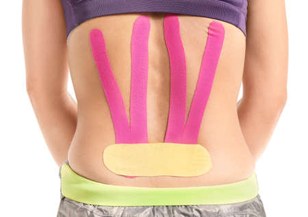 Sporty woman with physio tape applied on lower back against white background, closeup
