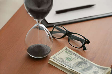 Hourglass with dollar banknotes on tableの写真素材