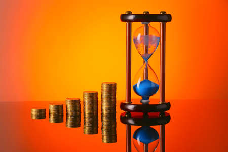 Hourglass with coins on color background