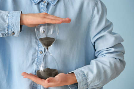 Woman with hourglass on color background, closeup