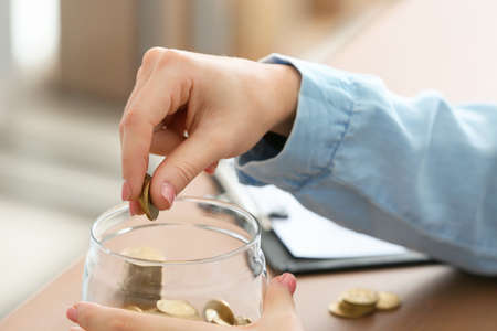 Woman putting coins into jar on table. Money savings concept