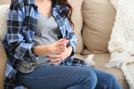 Sick pregnant woman measuring temperature at homeの写真素材