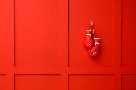 Pair of boxing gloves hanging on color wall