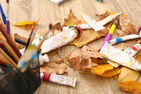 Tubes with paints and autumn leaves on table