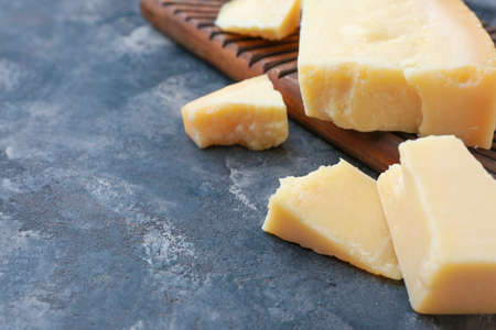 Board with tasty Parmesan cheese on gray background