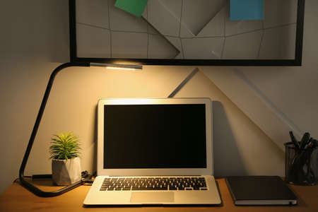 Comfortable workplace with modern laptop in evening