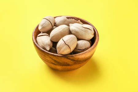 Bowl with tasty pecan nuts on color background