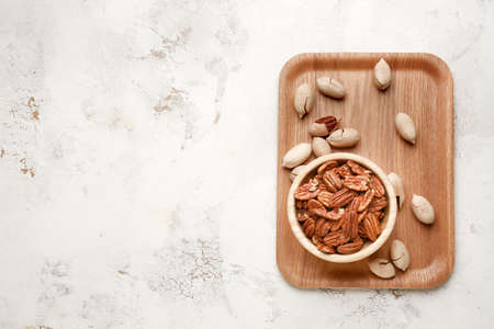 Bowl with tasty pecan nuts on light background