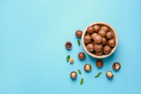 Bowl with tasty macadamia nuts on color background