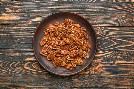 Plate with tasty pecan nuts on wooden background