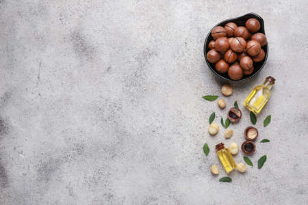 Tasty macadamia nuts with oil on gray background