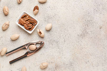 Bowl with tasty pecan nuts and nutcracker on light background