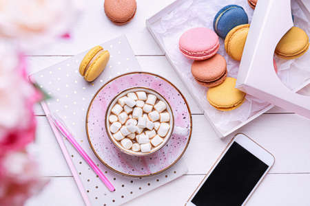 Cup of hot chocolate with tasty macarons and mobile phone on tableの写真素材